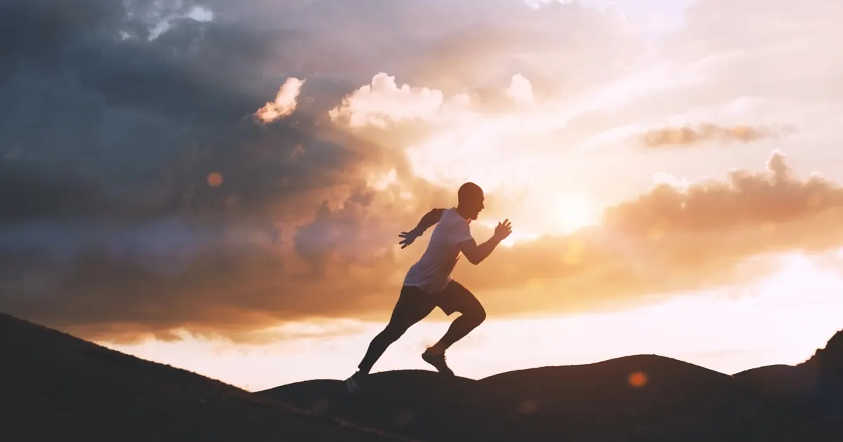Silhouette of a person running uphill under a dramatic sky