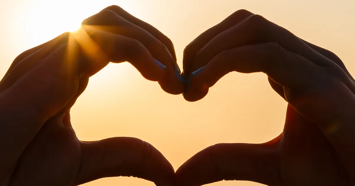 Hands forming a heart shape against the setting sun