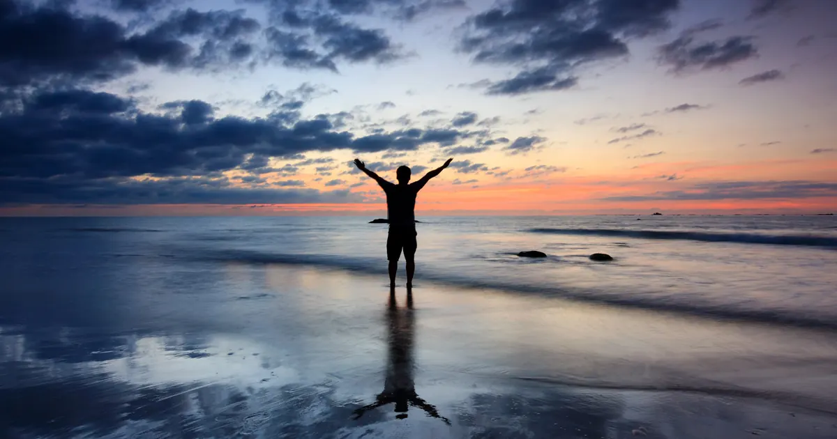 Improve Your Digestion with These Homeopathic Solutions Person with arms raised on a beach at sunset