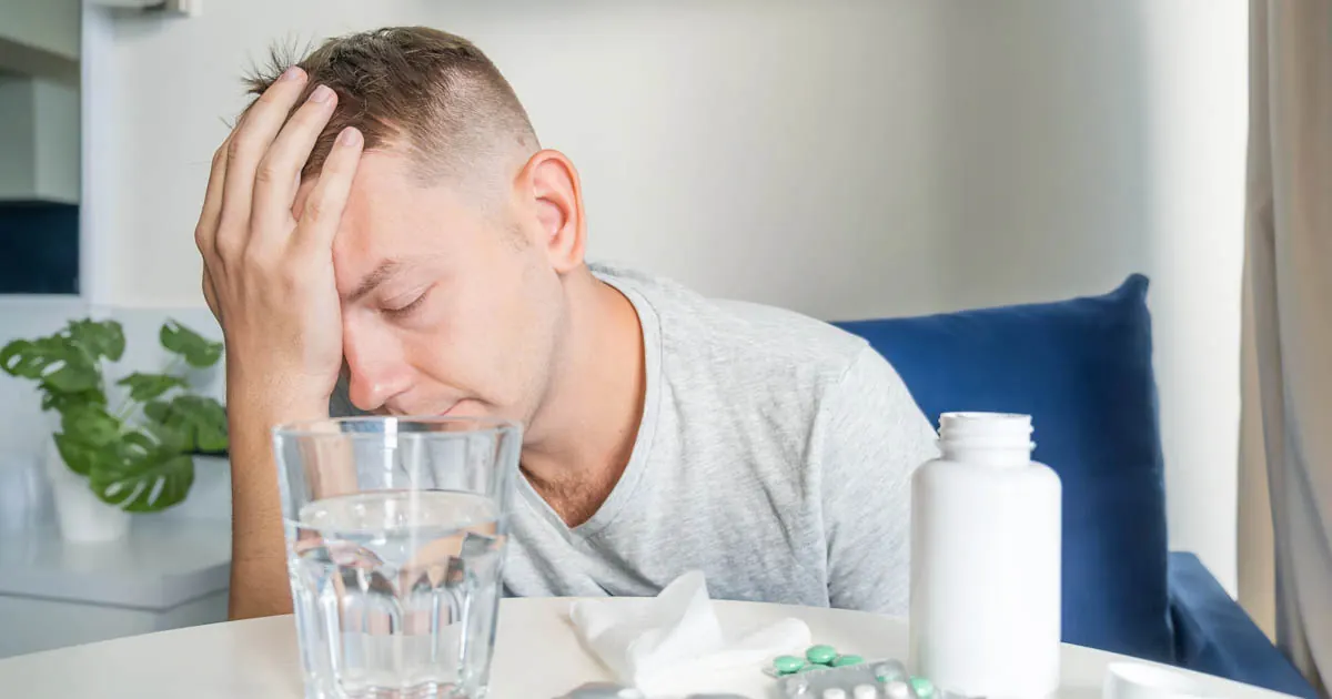 Exhausted man holding his head beside a glass of water and pill bottle